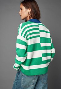 Grøn- og hvidstribet sweater med en blå krave, der har en strikket tekstur og en afslappet pasform, parret med falmede blå jeans.