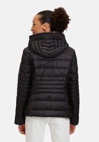 Svart puffjacka med huva, med quiltad textur, horisontell sömnad och en lätt rundad nederkant. Materialet verkar slätt och glänsande.