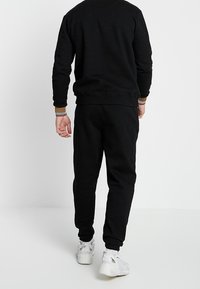 Set di felpa nera e pantaloni abbinati, caratterizzato da una texture morbida, polsini a coste e un design comodo. Sneakers bianche completano l'outfit.