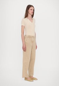 Beige ribbed short-sleeve polo top, high-waisted beige wide-leg trousers, and gold woven flats. Minimalist design with subtle texture.