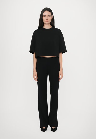 Schwarzes Crop-Top mit kurzen Ärmeln, kombiniert mit schwarzen weit geschnittenen Hosen. Glatter Stoff und minimalistisches Design, ohne sichtbare Muster oder Details.