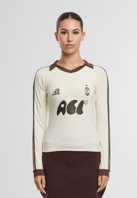 Kerman pitkähihaine paita ruskeilla yksityiskohdilla, kauluksella ja etuosassa painatuksella "ACi". Ominaisuuksiin kuuluu istuva muotoilu ja ribattu hihansuu.