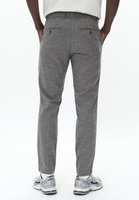 Pantalons gris en tissu texturé, dotés de deux poches arrière avec fermetures à bouton, associés à des chaussettes blanches et des chaussures de sport grises.