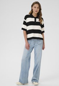 Zwart-wit gestreepte polo met korte mouwen, met een kraag en knopen, gecombineerd met lichtblauwe wijde jeans.