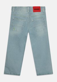 Jean en denim bleu clair avec une coupe droite, portant une étiquette rouge à la taille et deux poches arrière. Détails légèrement usés présents.