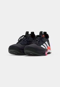 Chaussures de sport noires avec un dessus texturé, des rayures blanches et des accents roses. Caractéristiques d'un col rembourré et d'une semelle en caoutchouc pour une adhérence optimale.