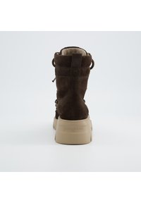 Bottine en suede marron avec un intérieur doux, semelle beige durable et lacets décoratifs. Équipée d'une languette pour un enfilage facile.