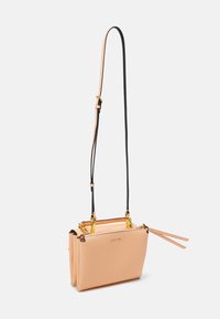 Mała beżowa skórzana torebka na ramię z regulowanym cienkim paskiem, złotymi okuciami i zamknięciem na zamek błyskawiczny z dwoma skórzanymi suwakami.