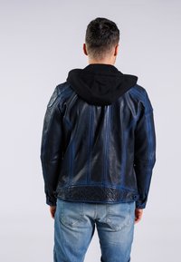 Skórzana kurtka z czarnym kapturem, z niebieskimi przeszyciami i pikowanym dolnym plecakiem. Noszona z jasnoniebieskimi dżinsami.