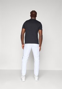 Sort t-shirt med korte ærmer parret med hvide bukser med grå sidestykker. Modellen vises fra ryggen. Glat stofstruktur.