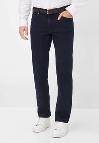 Donkerblauwe recht gesneden jeans met een klassiek vijf-pocket ontwerp, aangevuld met een brown leren riem en witte sneakers.