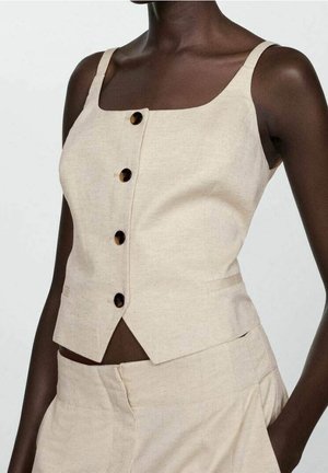 Vrouw draagt een beige mouwloze top met knopen en bijpassende hoge taillebroek met zakken, zichtbaar van schouders tot taille.