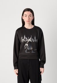 Sweatshirt preto com uma estampa de uma figura a caminhar em frente a um horizonte urbano. O material é suave, com um corte descontraído e punhos canelados.