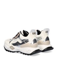 Zapatillas blancas gruesas con acentos plateados, lados texturizados, suela de goma negra y logo "EXÈ" en el talón. Diseño con cordones.