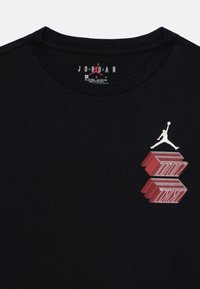 T-shirt en coton noir avec un logo Jumpman blanc et un design en blocs rouges audacieux sur la zone de la poitrine gauche. Encolure arrondie, manches courtes.