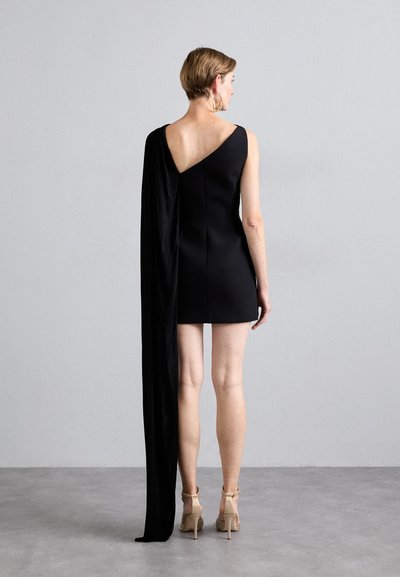 Juoda suknelė su vieno peties dizainu, ilgą, plazdantį apsiaustą iš vienos pusės, virš kelių ilgio ir giliu nugaros iškirpimu.