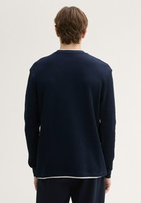 Maglietta a maniche lunghe a coste blu navy con scollatura a girocollo, vestibilità rilassata e spacchi laterali all'orlo, caratterizzata da un tessuto testurizzato e senza loghi visibili.
