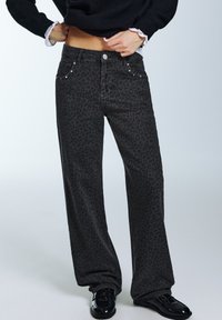 Svarta vida jeans med leopardmönster, framfickor och metallicnitar som detaljer. Slät denimstruktur med avslappnad passform.