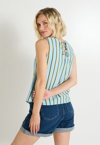 Top sin mangas de color azul claro con rayas verticales amarillas y verdes, con un escote en la espalda y un lazo decorativo. Combinado con shorts de mezclilla oscuros.