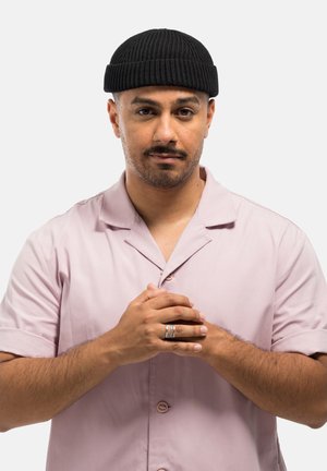 Black ribbed beanie, light pink button-up shirt with short sleeves, person clasping hands, smooth texture, neutral background.