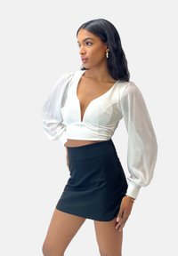 Blouse blanche courte avec manches bouffantes, décolleté en V profond, associée à une mini-jupe noire cintrée. Texture de tissu lisse, design élégant.