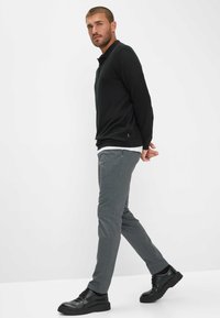 Polo a maniche lunghe nera, pantaloni grigi a fantasia e scarpe nere. L'outfit presenta un design semplice con hardware e dettagli minimi.