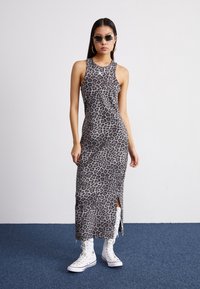 Maxi dress grigio con stampa leopardata, design senza maniche e spacchi laterali, abbinato a sneakers alte bianche. Tessuto liscio e leggermente elasticizzato.
