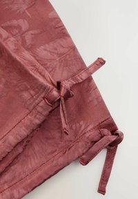 Rosa tyg med ett strukturerat bladmönster. Knyts vid hörnen för stängning. Slät yta med en subtil glans.