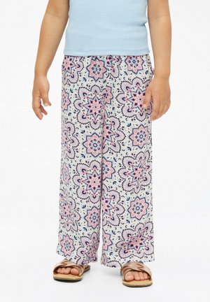 Enfant portant un pantalon blanc à jambes larges avec des motifs floraux roses et bleus, un débardeur bleu clair et des sandales dorées sur un fond blanc.