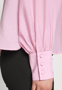 Camicia a maniche lunghe di colore rosa chiaro con design di maniche arricciate e dettaglio del polsino a tre bottoni, realizzata in tessuto testurizzato.