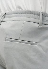 Lysegrå tilpassede bukser med sidelomme, beltehemper og et lett stoffbelte festet rundt midjen.