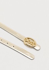 Ασημένια μεταλλική ζώνη με λαμπερό φινίρισμα, με χρυσή οβάλ αγκράφα που φέρει τη λέξη «BOSS» με γράμματα κομμένα.