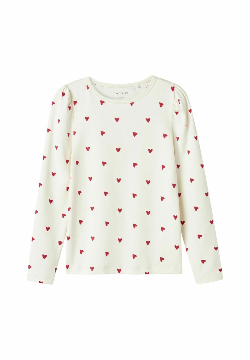 Haut à manches longues en coton écru avec un motif de cœurs rouges dispersés. Texture douce avec des coutures d'épaule froncées et un col rond.