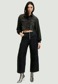 Černá zkrácená denimová bunda s knoflíkovým zapínáním a dvěma náprsními kapsami, spárovaná s černými kalhotami s vysokým pasem a širokými nohavicemi, a stříbrnými botami na podpatku.