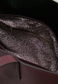 Borsa bordeaux con una texture esterna liscia, caratterizzata da una fodera a motivo floreale in marrone chiaro e crema. Include una tasca con zip all'interno.