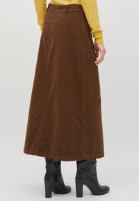 Jupe maxi marron en tissu doux, avec une forme droite et des poches latérales. Assortie à des bottes noires à talons.