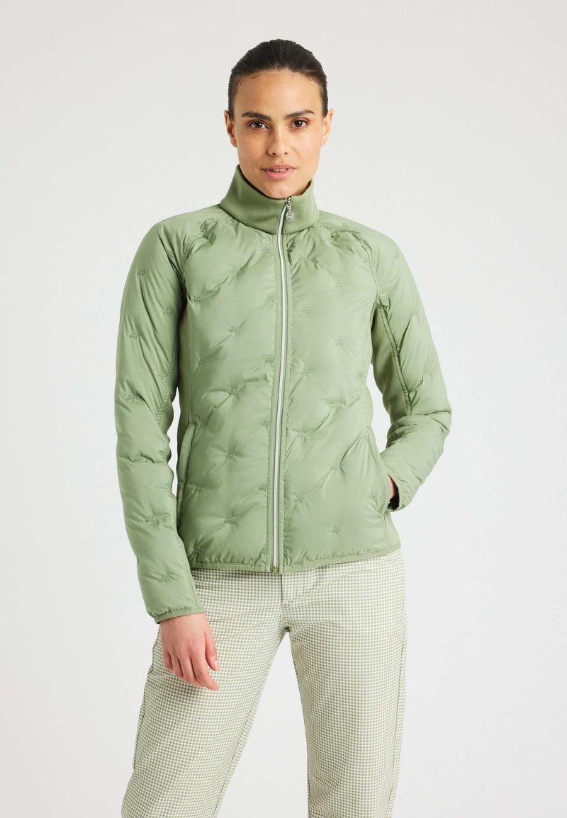 Chaqueta de plumas verde claro con un cuello alto, cierre frontal y un patrón texturizado. Combina con unos pantalones a cuadros, mostrando un diseño ajustado.
