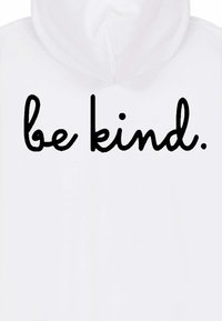 Bela jopa s kapuco z motivom črnega pisave v kurzivi, na kateri piše "bodi prijazen." Besedilo je osredotočeno in izstopajoče, z gladko teksturo tkanine.