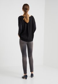 Top negro de manga larga, con dobladillo curvado, combinado con jeans gris de corte ajustado. La modelo lleva unos zapatos bajos azules; el cabello recogido, vista desde atrás.