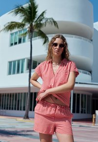 Piros-fehér csíkos rövid ujjú ing és rövidnadrág szett, könnyű anyagból készült, az ing elején zsebbel és rugalmas derékpánttal.