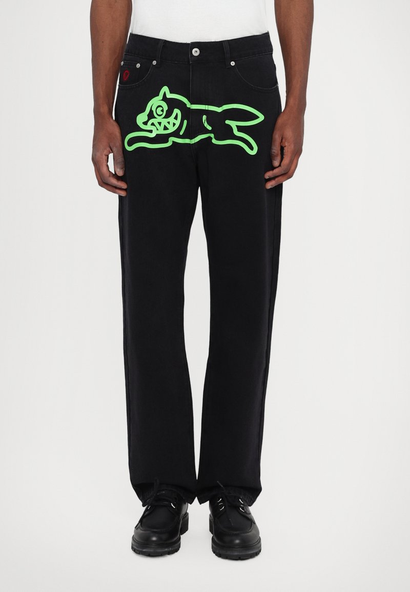 Black denim pants with a relaxed fit, featuring a large neon green graphic of a cartoon cat on the front. Black shoes complete the outfit.