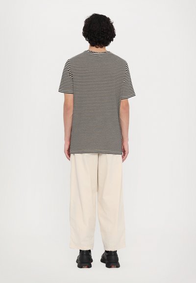 Tricou cu dungi negre și albe, cu mâneci scurte, asortat cu pantaloni largi bej deschis și pantofi negri. Design simplu și casual.