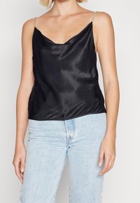 Camisole en satin noir avec un décolleté bénitier, des bretelles fines argentées et une coupe décontractée. Associée à un jean en denim bleu clair.