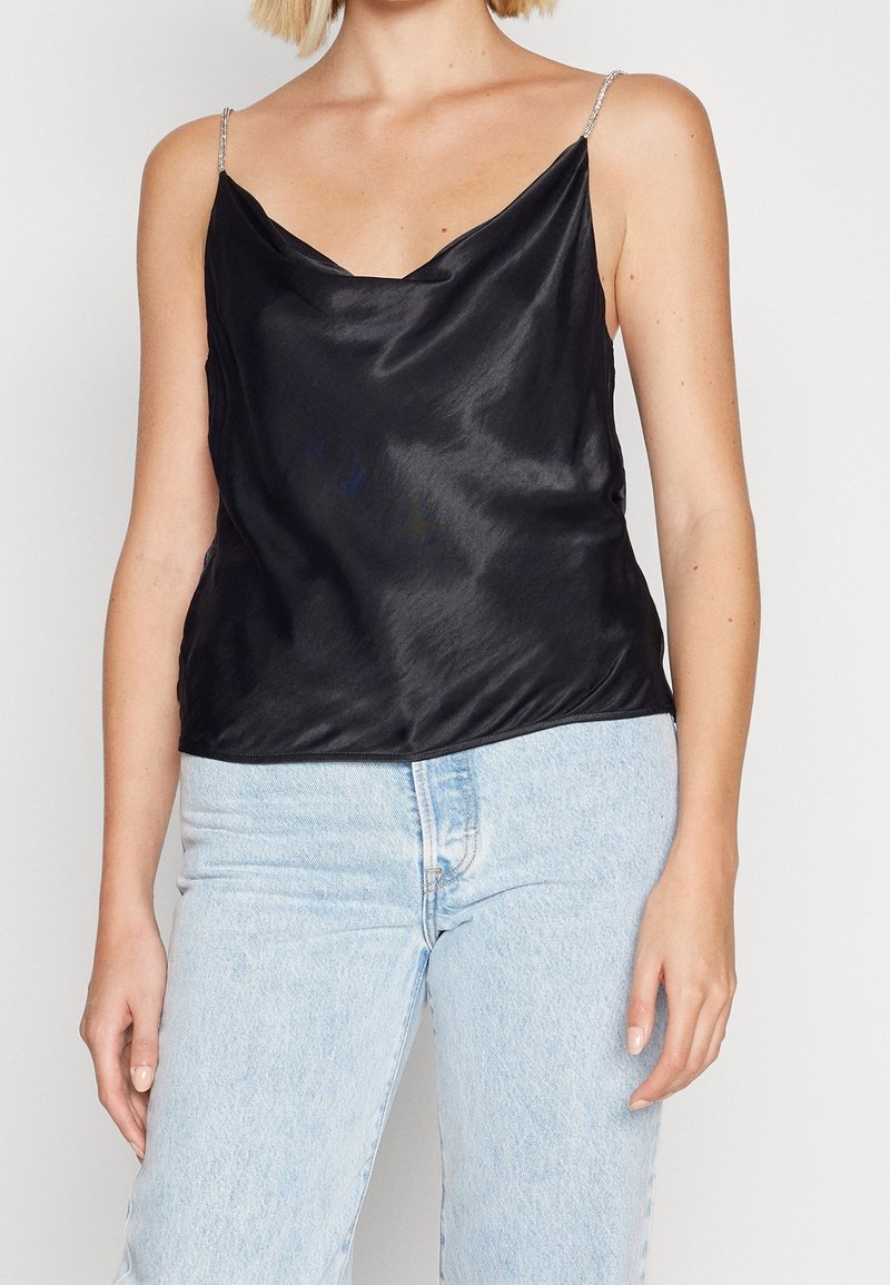 Camisole en satin noir avec un décolleté bénitier, des bretelles fines argentées et une coupe décontractée. Associée à un jean en denim bleu clair.