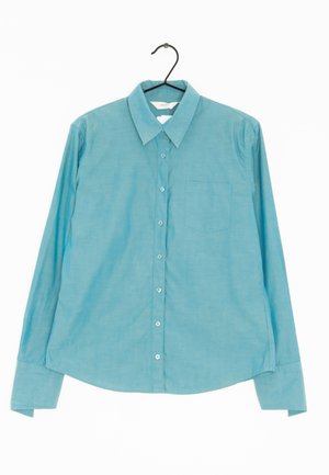 Camicia button-up a maniche lunghe di colore azzurro chiaro con colletto, taschino sul petto e una leggera texture. Bottoni sulla parte anteriore.