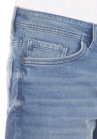 Jeans de mezclilla azul claro con un acabado desgastado, que cuentan con un bolsillo frontal, costuras visibles y una textura suave.