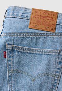 Poche arrière de jeans Levi's bleu clair avec une étiquette en cuir marron indiquant la marque, le numéro de lot 501 et la taille W32 L32 avec un détail cousu.