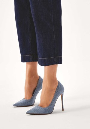 Helle blaue Denim-Pumps mit spitzem Zeh, schlankem Stilettoabsatz und glatter Textur. Kombiniert mit dunkelblauen, verkürzten Jeans.
