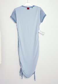 Robe bleu clair à manches courtes avec fronces latérales et manches en chambray suspendue sur un cintre en plastique transparent sur fond blanc.