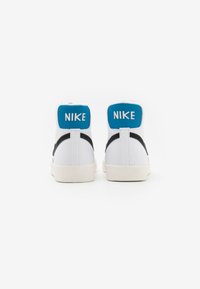 Vita höga sneakers med svarta accenter och blå vadderade kragar, med Nike-logotypen i vitt på baksidan. Gummisula.